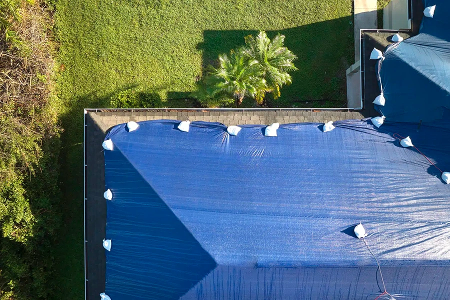 Aerial view of a blue emergency tarp secured over a damaged roof