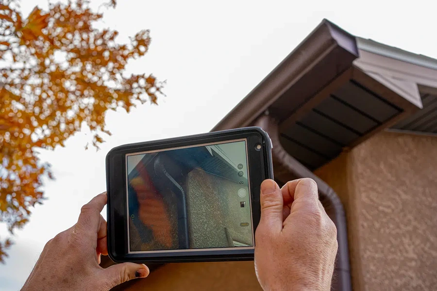Roof inspector photographing a home's roofline and gutters on a tablet during an inspection
