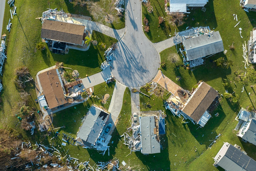 Aerial view of a neighborhood with storm-damaged roofs and scattered debris