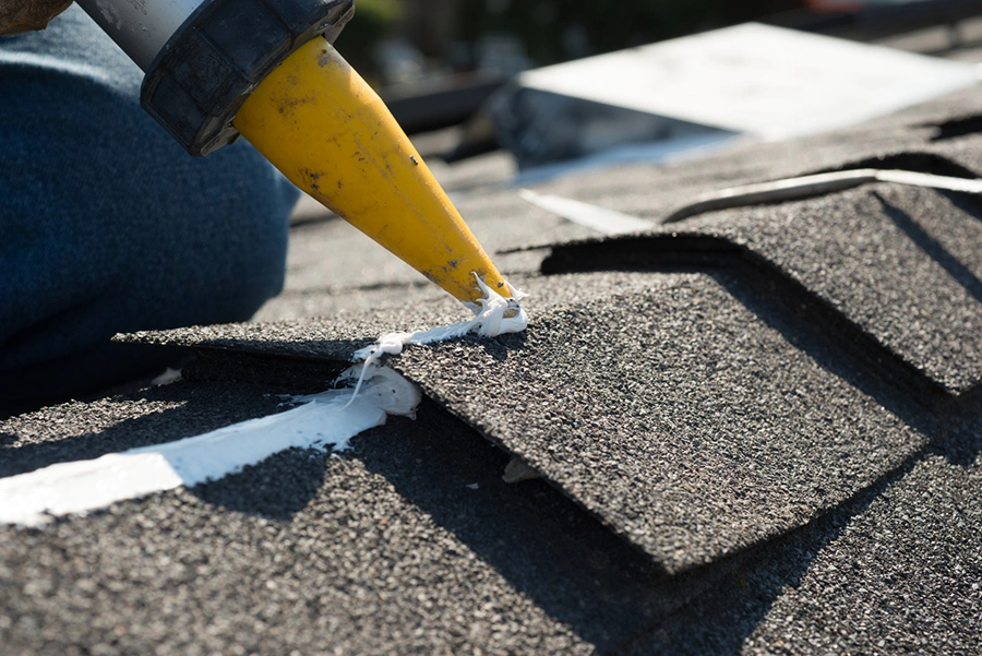 Roofer applying sealant along a shingle edge with a caulking gun