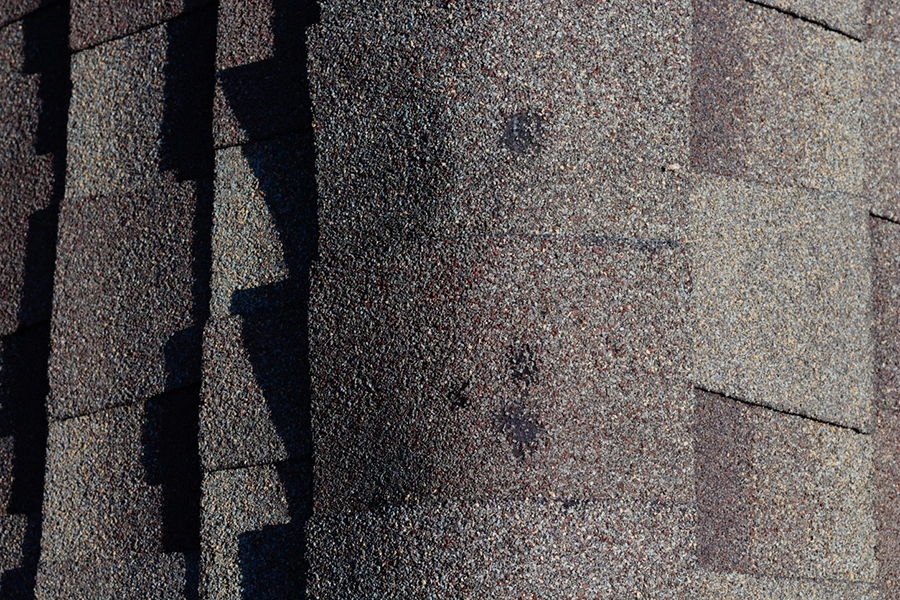 Creased and torn asphalt shingles across a wind-damaged roof slope