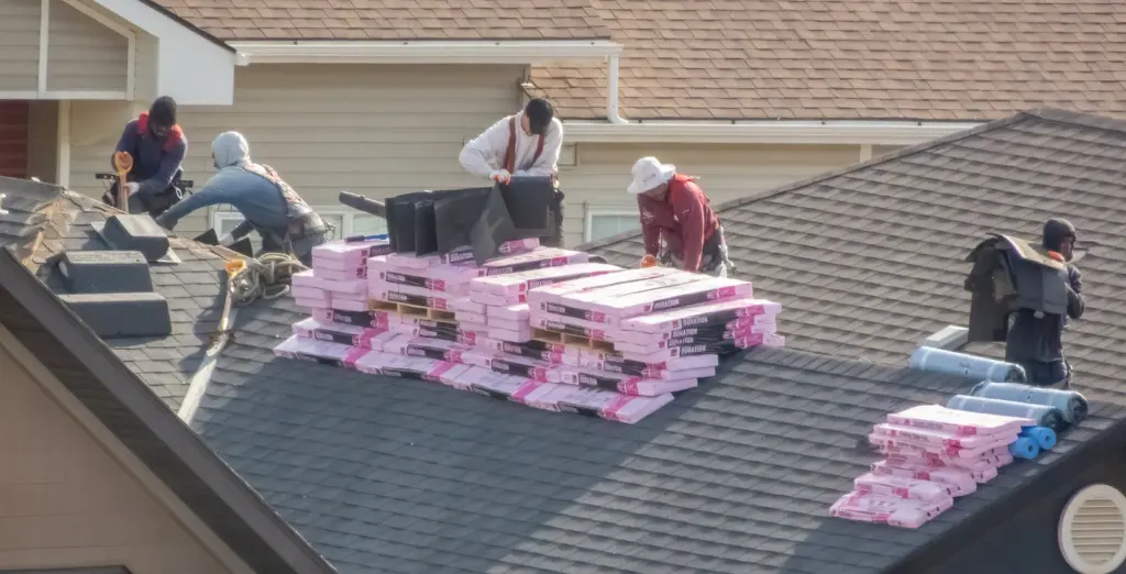 Roofing crew staging bundles of shingles across a roof before installation