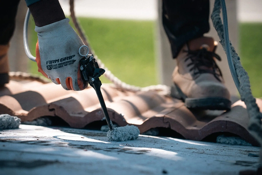 Roofer applying sealant while re-bedding ridge caps on a tile roof