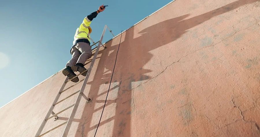 Roofer on a ladder working along a steep commercial roof slope