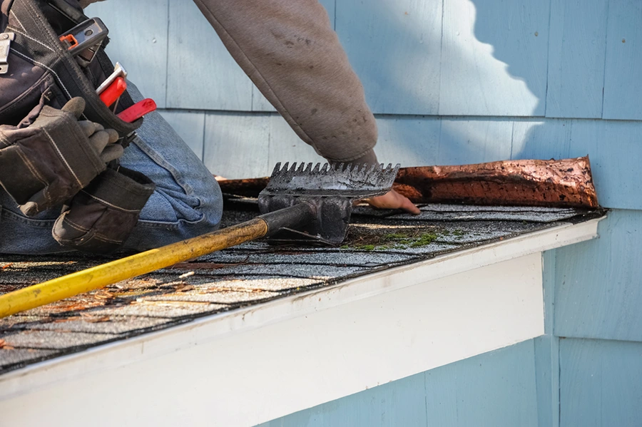 Roofer prying away damaged fascia and gutter boards during storm repairs