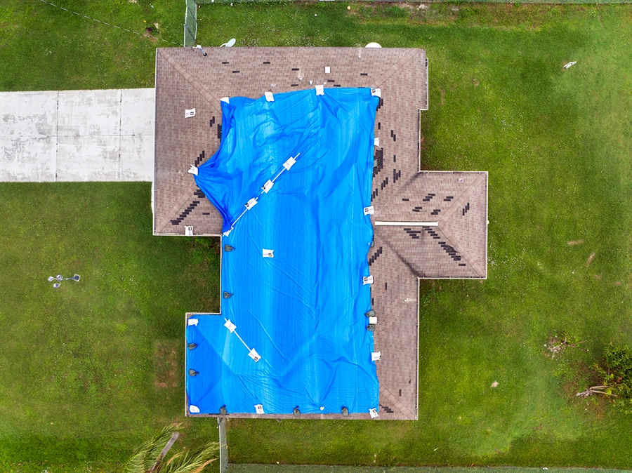 Aerial view of a blue emergency tarp covering a storm-damaged roof