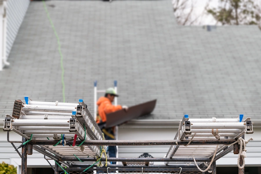 Roofing crew working from ladders while replacing a storm-damaged roof