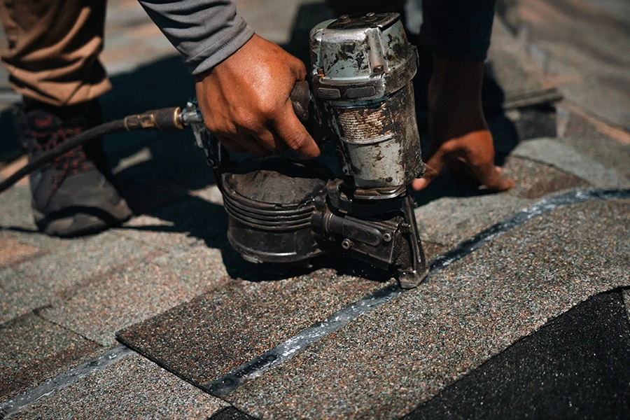 Roofer using a nail gun to secure shingles during a leaking roof repair