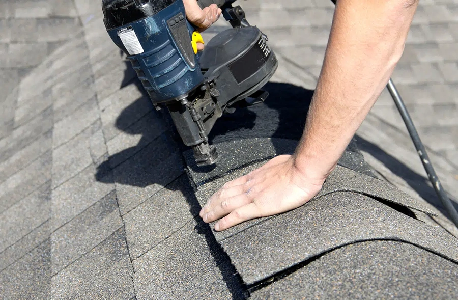 Close-up of a roofer nailing asphalt shingles during a roof repair