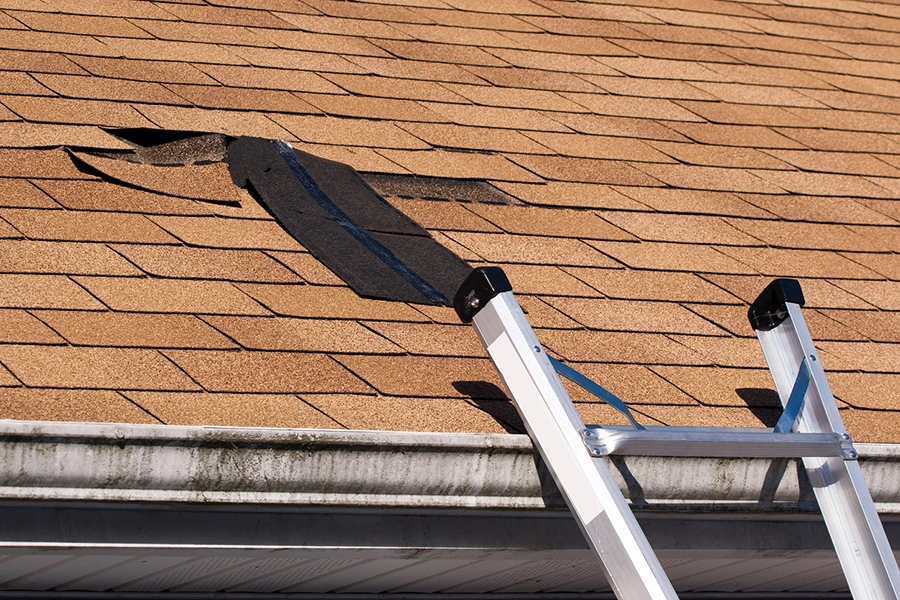 Ladder against a roof with shingles torn away by storm winds