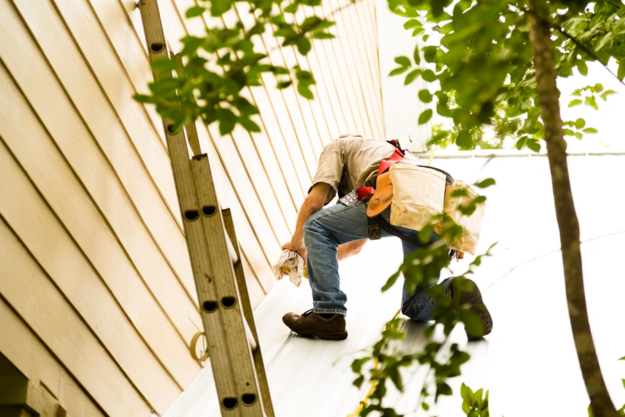 Worker on a ladder repairing siding and trim after storm damage