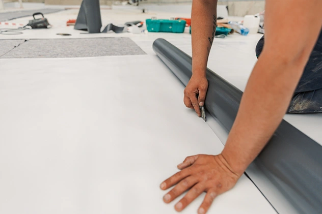 Roofer unrolling white PVC single-ply membrane during a flat commercial roof installation