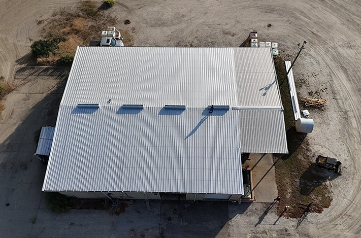Aerial view of a white commercial metal roof on a Florida warehouse building with a roofer at work