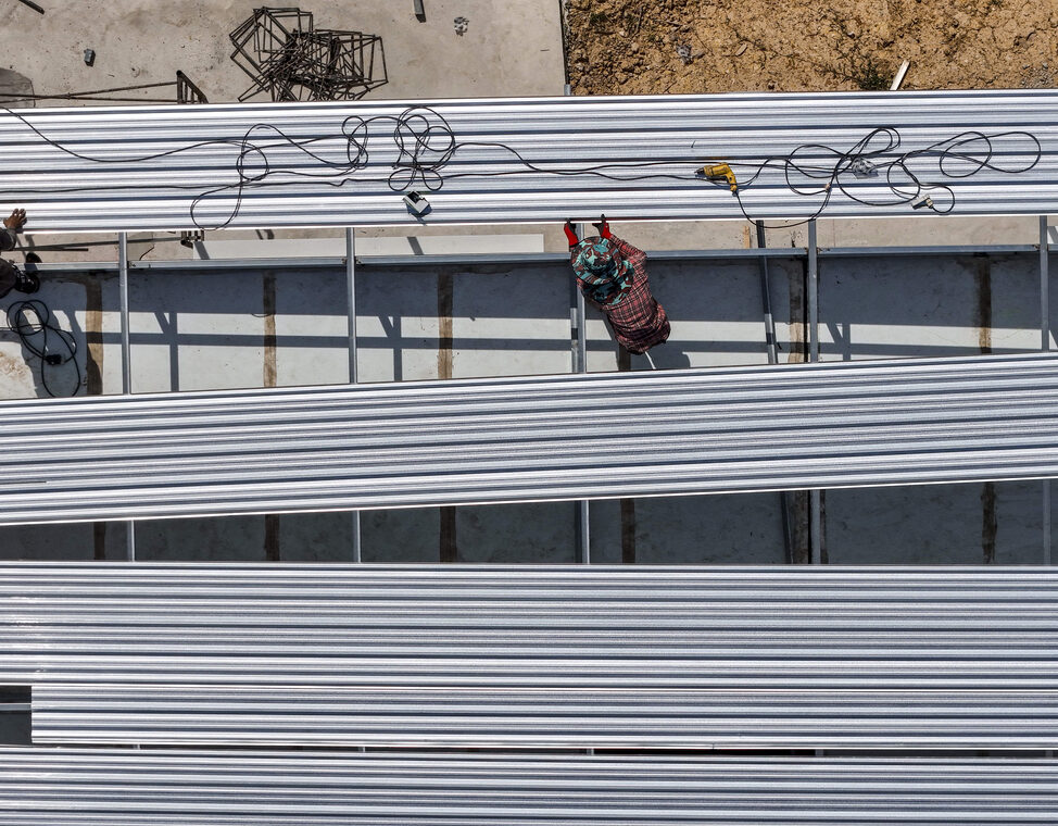 Aerial view of construction workers installing roofing panels on a building, surrounded by tools and materials, showcasing teamwork, precision, and the construction process in progress.
