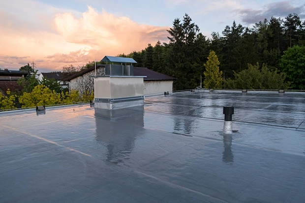 Flat membrane roof with rooftop vents and ductwork on a commercial building at dusk