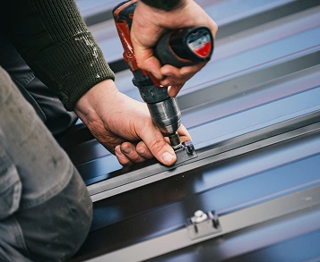 Roofer using a cordless drill to fasten a standing seam metal roof panel
