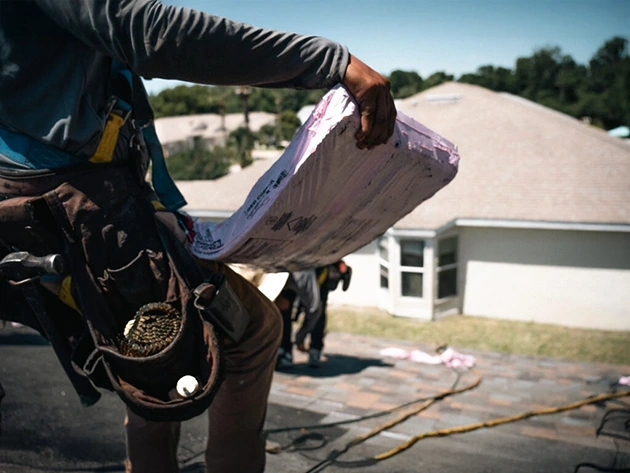 Roofer carrying a bundle of shingles across a Florida home during storm restoration work
