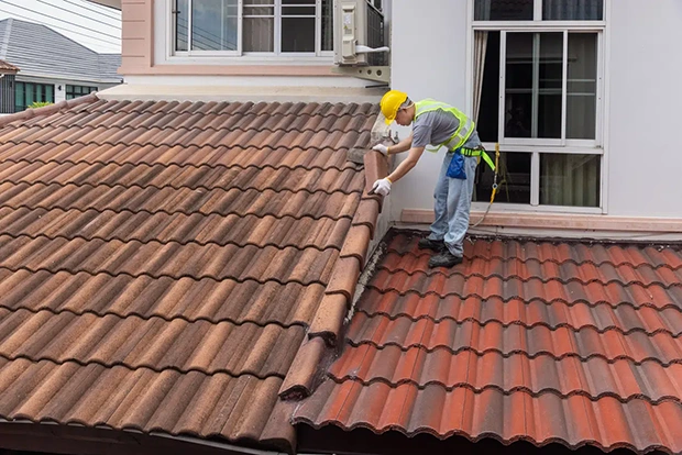 Roofer in a safety harness repairing mortar along the ridge line of a clay tile roof